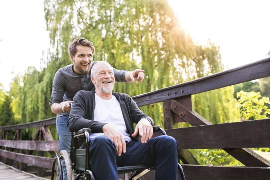 Hipster son walking with disabled father in wheelchair at park.