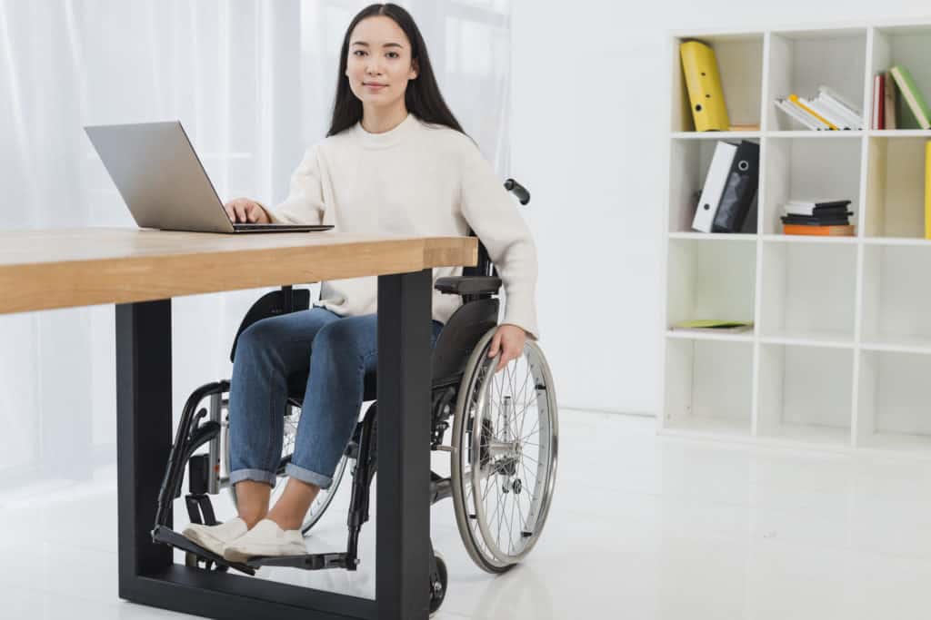 asian woman in a wheel chair sitting at a desk working on a laptop